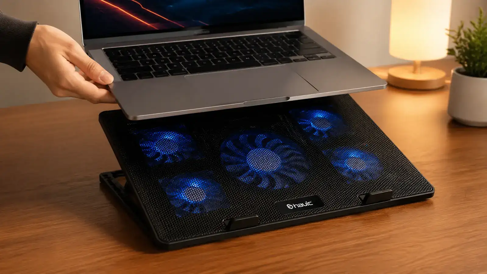 Hand placing a laptop onto a Havit cooling pad with the fans visible through the mesh surface